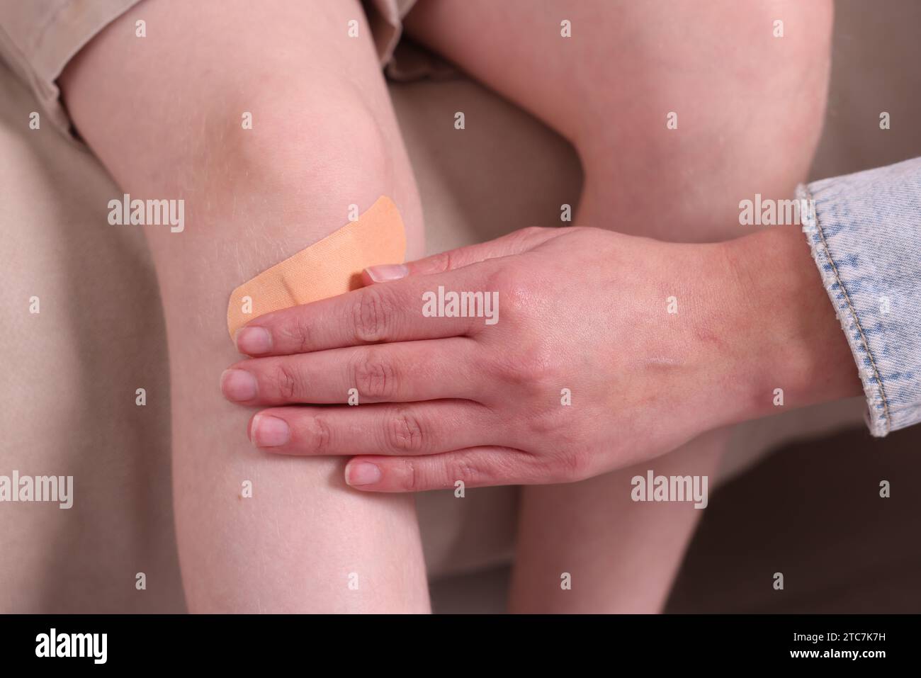 Woman putting sticking tape onto little boy`s knee on sofa, closeup